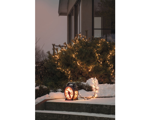 Conifère décoré avec guirlande lumineuse et lanterne sur un escalier dans la neige.