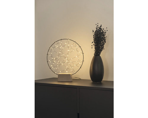 Dekorative Tischleuchte mit abstrakten Lichtpunkten neben einer Vase auf einem Schrank