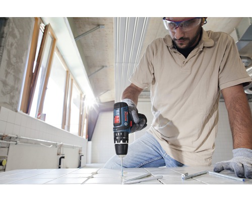 Un artisan perce un trou dans un carreau avec une perceuse.