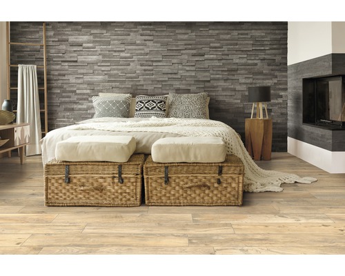 Schlafzimmer mit Steinwand, Holzboden und geflochtenen Truhen vor dem Bett