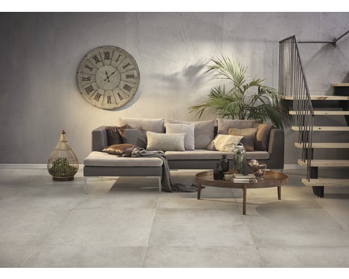 Salon avec canapé, table basse, horloge et escalier dans un intérieur avec un sol carrelé.