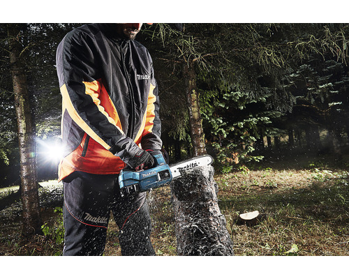 Une personne utilise une tronçonneuse sans fil Makita pour couper un tronc d''arbre à l''extérieur.