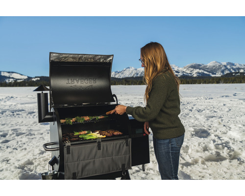 Frau grilliert auf einem Traeger Grill im Schnee mit Bergen im Hintergrund.