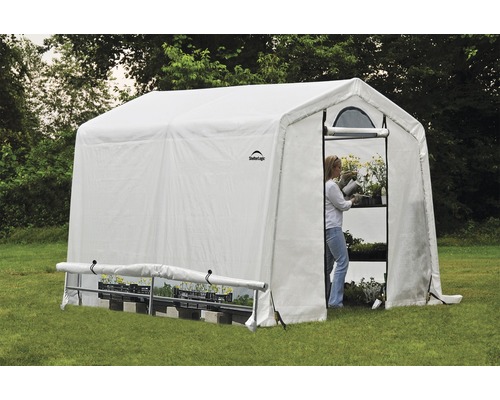 Serre avec étagères et une femme arrosant des plantes