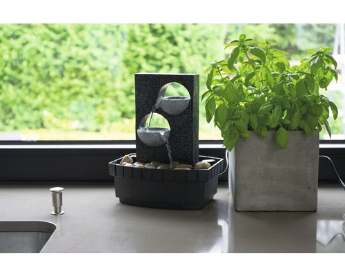 Fontaine d''intérieur décorative en pierre avec deux vasques et un pot de basilic sur un plan de travail