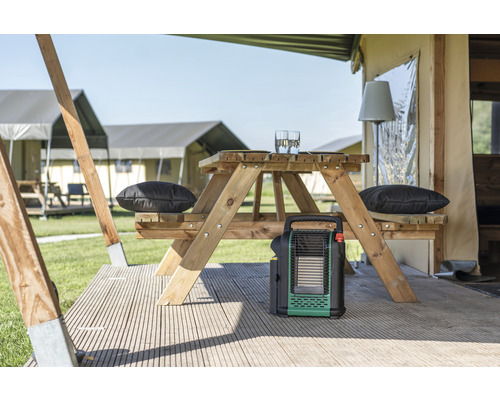 Scène avec un radiateur portable, une table en bois avec des coussins et des verres sur une terrasse devant des tentes.