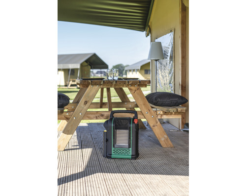 Scène de camping avec table de pique-nique, chauffage de camping et tentes en arrière-plan.