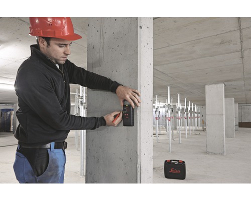 Mann mit Bauhelm markiert eine Betonwand mit einem Messgerät und einem Stift. Im Hintergrund befindet sich ein Baustellenbereich mit Stützen und einer Werkzeugkiste. Leica Logo.