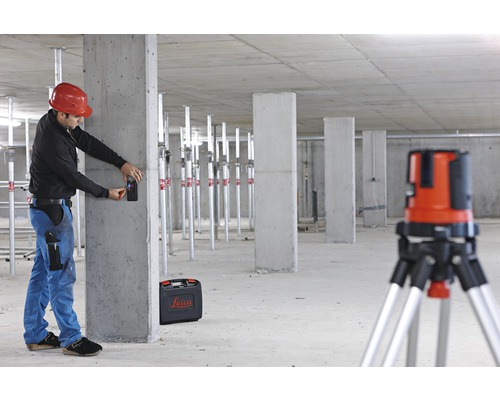 Ein Mann mit Schutzhelm benutzt einen Laser-Entfernungsmesser in einem Rohbau mit Betonpfeilern und einem Rotationslaser auf einem Stativ