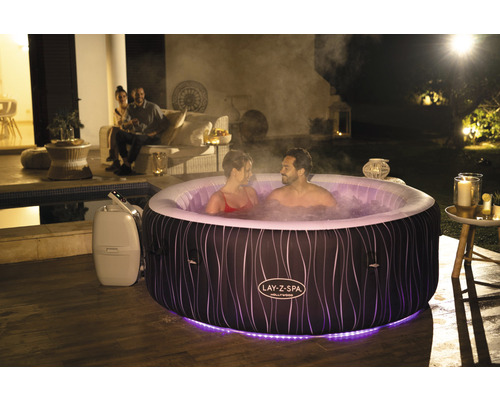 Jacuzzi gonflable Lay-Z-Spa avec deux personnes dans l''eau dans un jardin la nuit.