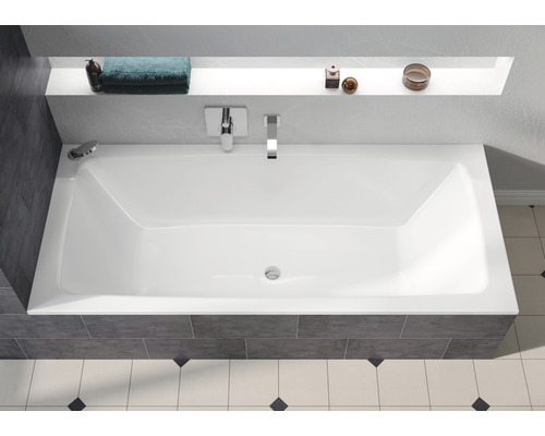 Baignoire rectangulaire dans une salle de bains avec robinetterie et étagère