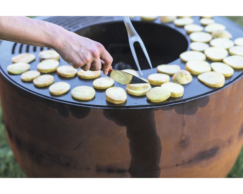 Personne faisant cuire des pommes de terre sur un foyer extérieur avec des ustensiles de cuisine.