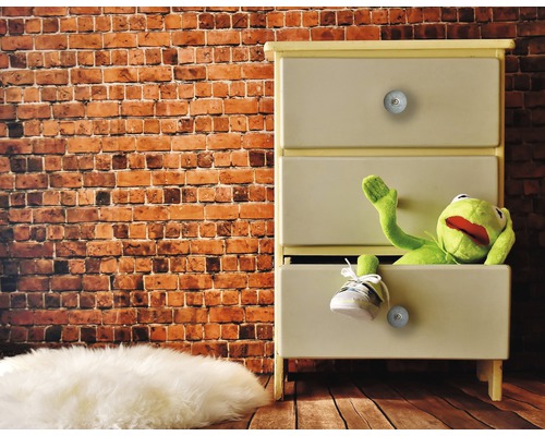 Commode à trois tiroirs avec une poupée en tissu et une chaussure devant un mur de briques