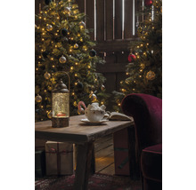 Scène de Noël avec sapins décorés, table avec lanterne, tasse et cadeaux