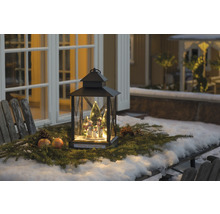 Lanterne de Noël décorative avec figurines de bonhomme de neige et branches de sapin sur une table à l''extérieur.