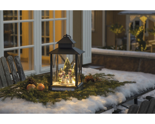 Lanterne de Noël décorative avec figurines de bonhomme de neige et branches de sapin sur une table à l''extérieur.