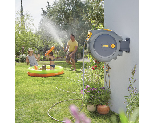 Une famille utilise un dévidoir automatique de Hozelock pour arroser et jouer dans le jardin.