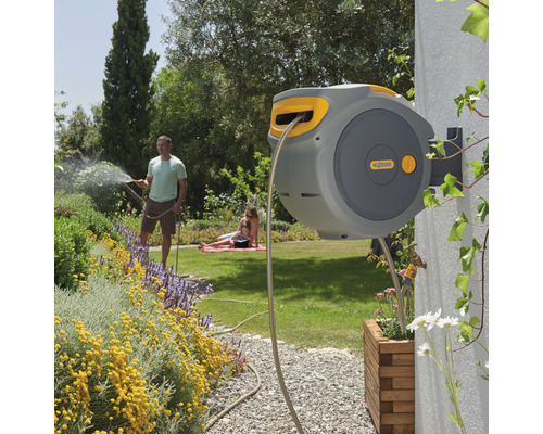 Bobine de tuyau automatique sur un mur de maison avec un homme arrosant le jardin