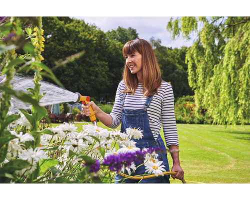 Une femme arrose des fleurs dans le jardin avec un tuyau d''arrosage.