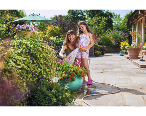 Une femme et une fille arrosent des fleurs avec un tuyau d''arrosage dans le jardin.