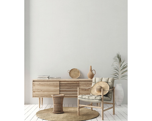 Helles Wohnzimmer mit Holzkommode, Sessel, Strohhut und Dekorationen auf einem runden Teppich.