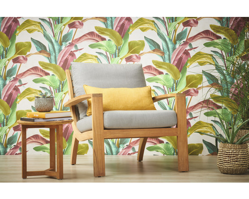 Gartenszene mit Sessel, Kissen und Beistelltisch vor einer gemusterten Tapete