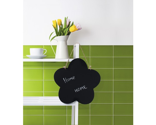 "Dekorative Szene mit Blumen, Tasse und Blume-förmiger Tafel mit dem Text ""Home"" auf einem Regal vor grünen Fliesen."