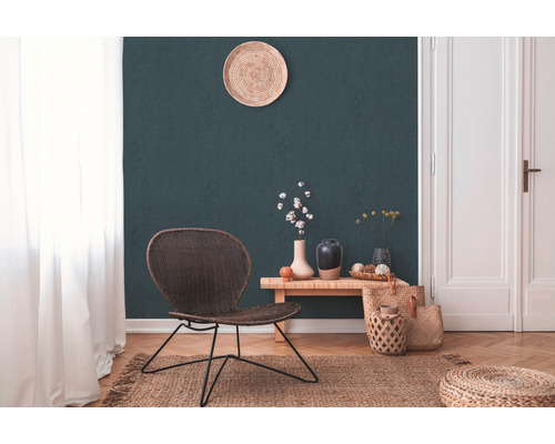 Wohnzimmer mit Rattansessel, Holztisch, Vasen, Juteteppich und Dekoration vor dunkelgrüner Wand