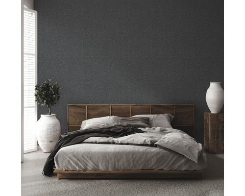 Chambre avec lit, tête de lit en bois, plante en pot et vase sur un socle en bois devant un mur texturé