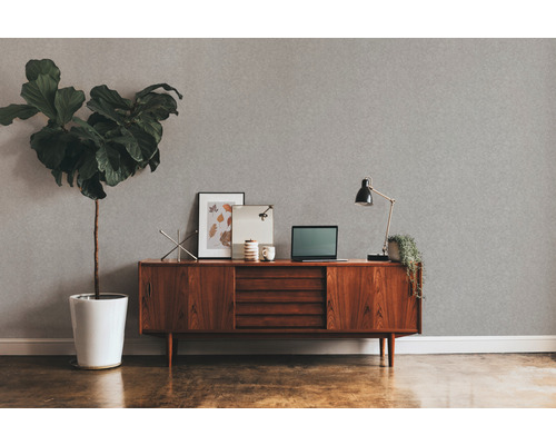 Wohnzimmer mit grauer Strukturtapete, Holzkommode, Zimmerpflanze und Schreibtischlampe.