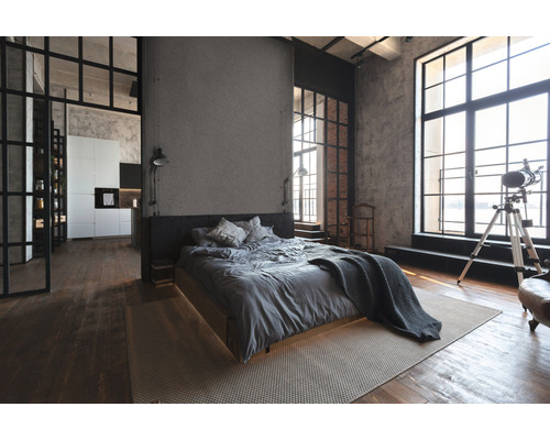 Innenaufnahme eines Schlafzimmers im Loft-Stil mit Bett, Fenstern und Holzboden.