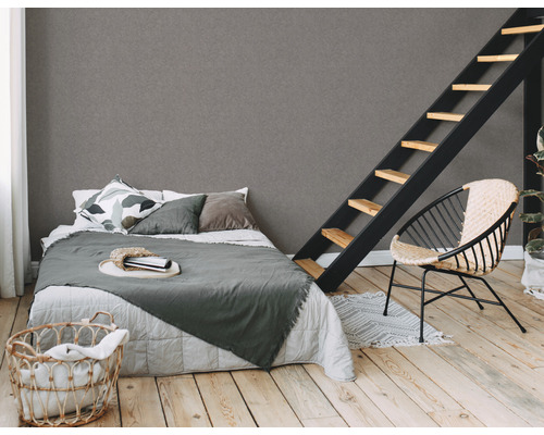 Schlafzimmer mit Bett, Leiter und Korbsessel auf hellem Holzboden vor einer grauen Wand