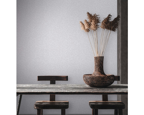 Szene mit Tisch, Stühlen, Vase und Dekoration vor einer hellen Wandtapete.