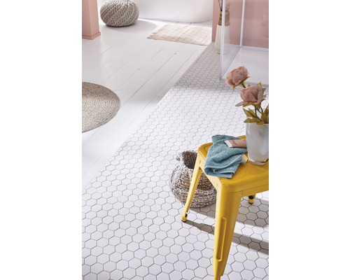 Salle de bains avec carrelage de sol hexagonal blanc, tabouret jaune, serviette et accessoires de salle de bains.