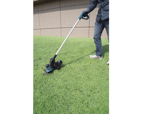 Une personne utilise un coupe-bordures à batterie dans le jardin.