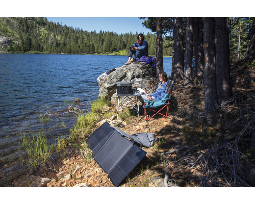 Scène au bord du lac avec panneau solaire portable, centrale électrique, table et chaises de camping pour une utilisation en extérieur.