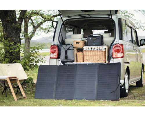 Scène avec un panneau solaire devant un coffre ouvert de voiture avec équipement de camping.