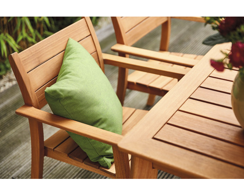 Scène de jardin avec table et chaises en bois, un coussin vert et des fleurs dans un vase.
