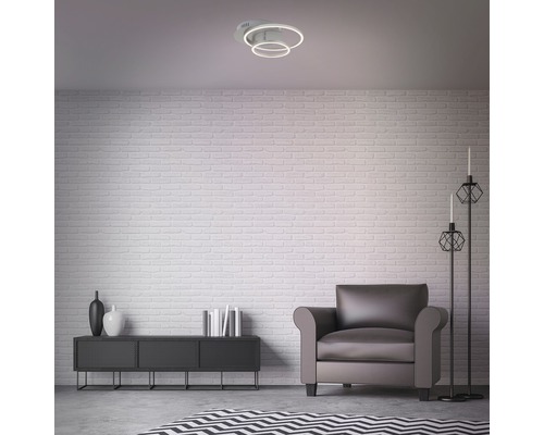 Salon avec plafonnier, fauteuil et commode devant un mur de briques.