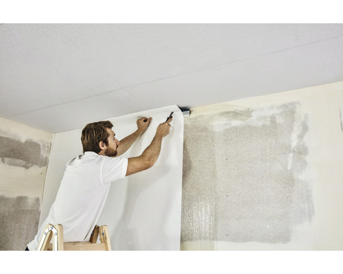 Ein Mann auf einer Leiter bringt eine Tapete an der Wand an