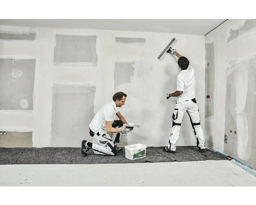 Deux artisans enduisent un mur dans une pièce.