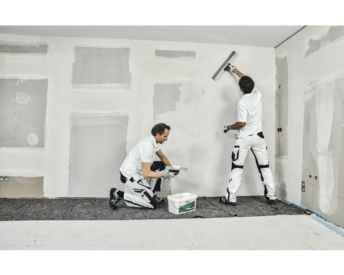 Deux artisans enduisent un mur à l''intérieur.