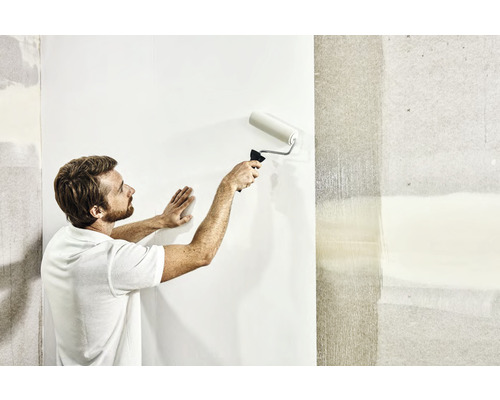 Un homme tapisse un mur avec un rouleau à peinture.