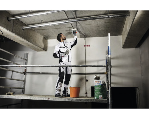 Un artisan sur un échafaudage enduit un plafond. Un sac de mastic et un seau sont posés sur l''échafaudage.