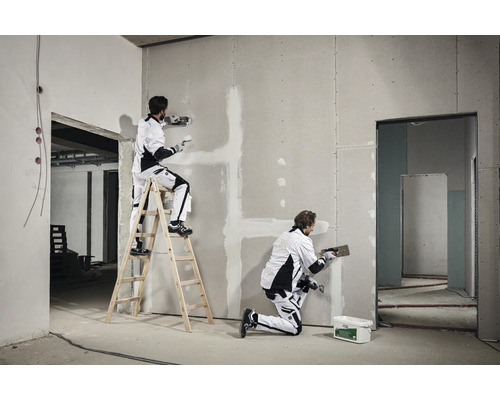 Deux artisans enduisent un mur en plaques de plâtre dans un bâtiment en construction.