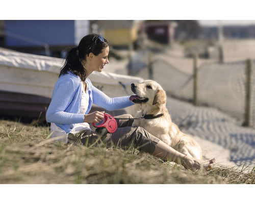 Frau streichelt Hund mit Rollleine am Strand
