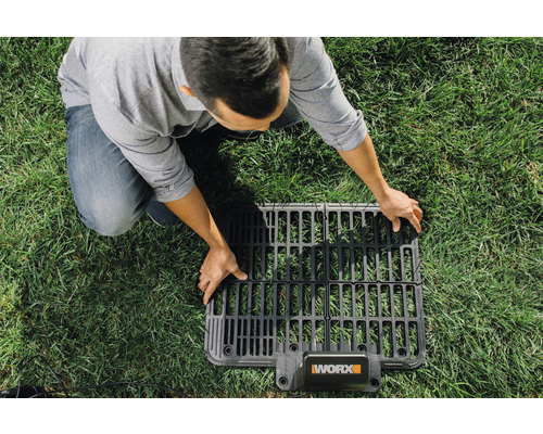 Un homme pose une grille de câble périphérique pour robot tondeuse WORX sur une pelouse
