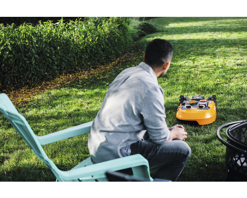 Mann im Gartenstuhl betrachtet einen Rasenmähroboter auf einer Rasenfläche