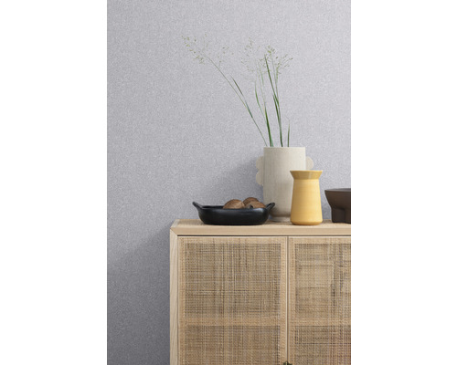 Gemusterte Tapete über einem Schrank mit Rattanfront, darauf Vasen und eine Schale