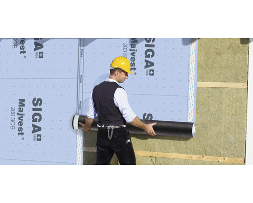 Un homme fixe un écran de façade SIGA Majvest sur un mur de maison avec isolation thermique.